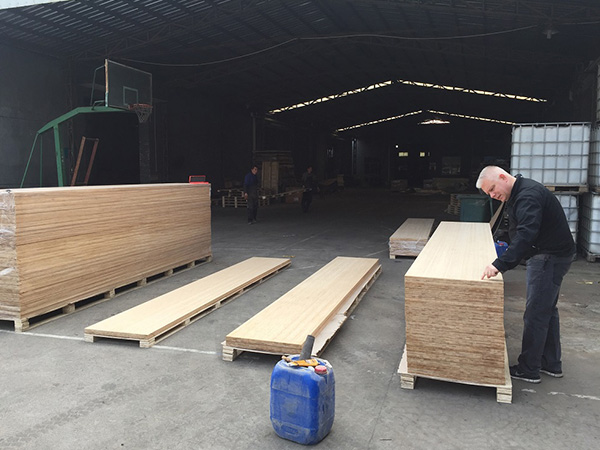 Foreign inspector inspecting bamboo panel thickness and lamination quality in workshop